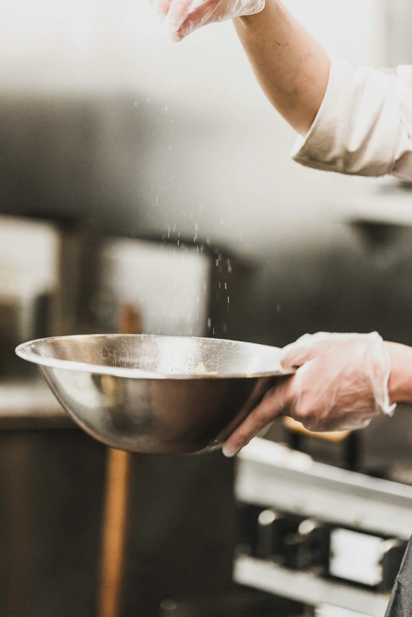 Hands seasoning food in a working kitchen