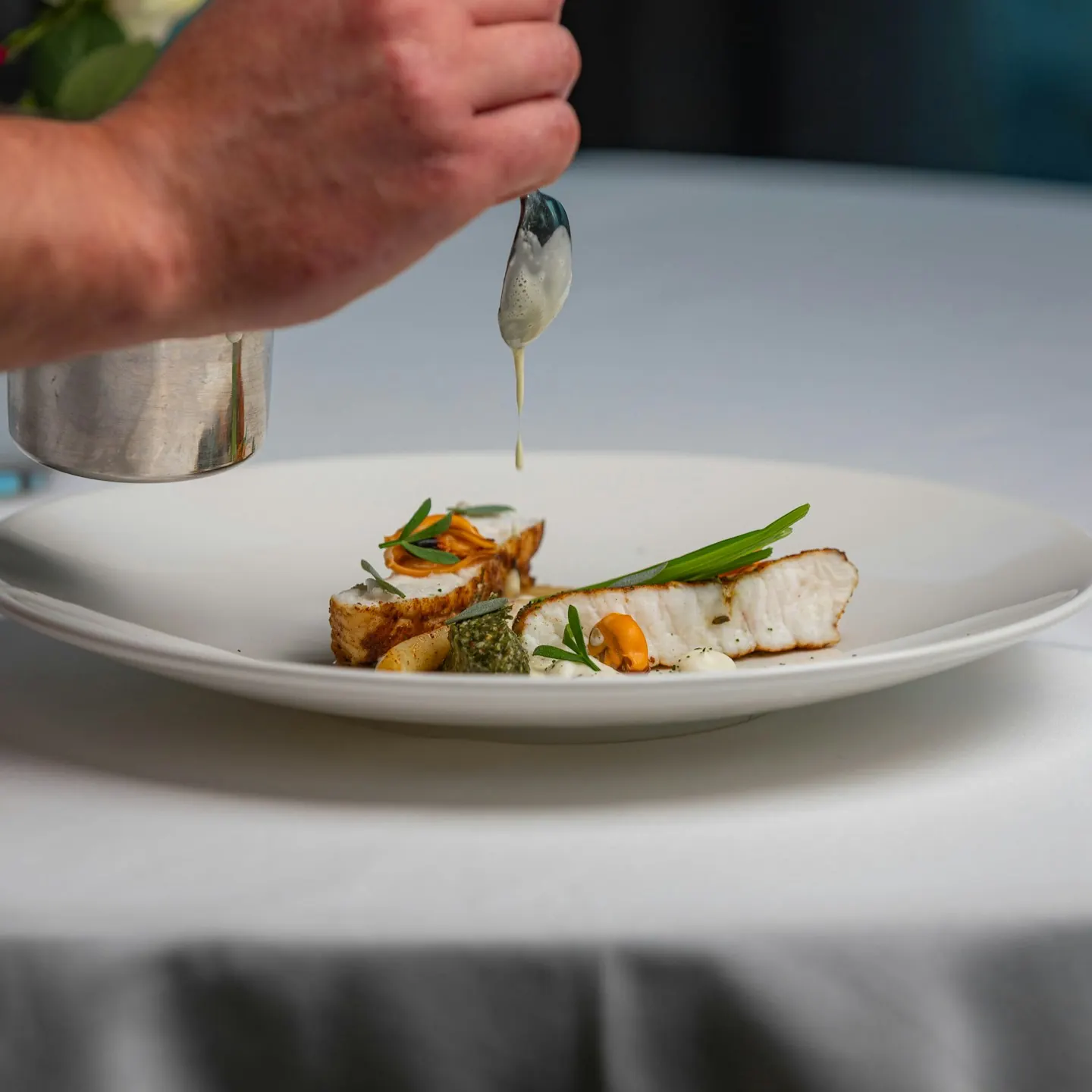 A cook finishing a plated fish dish