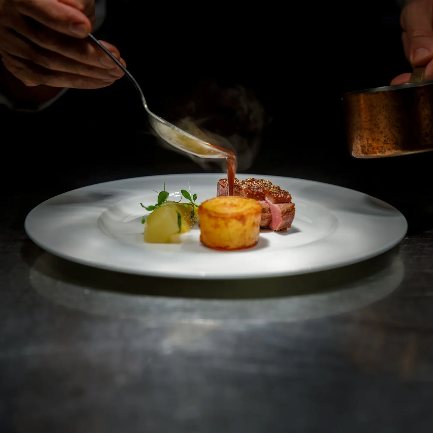 Chef pouring sauce over a plated steak